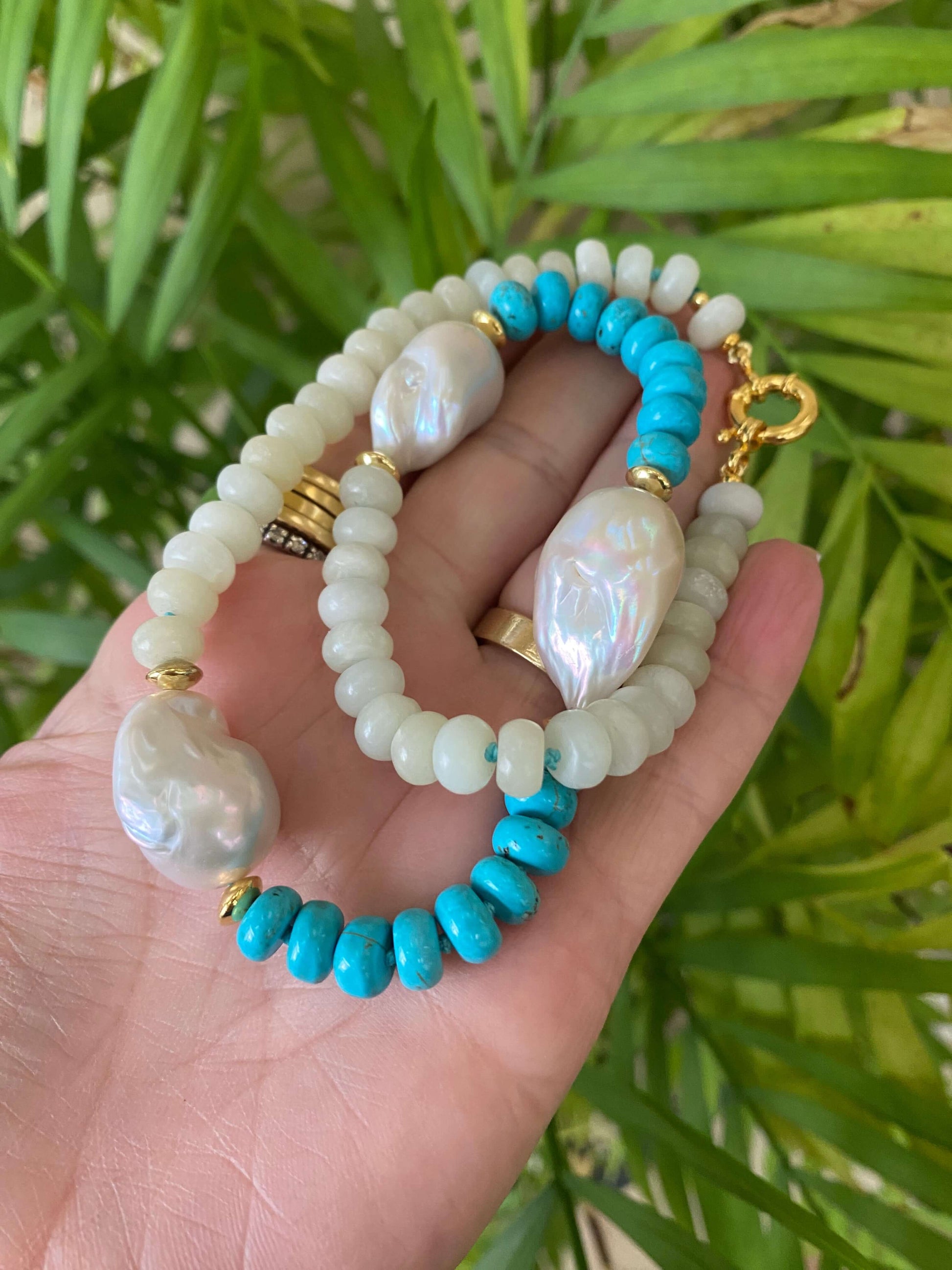 Hand holding green jade and turquoise pearl necklace against leafy backdrop