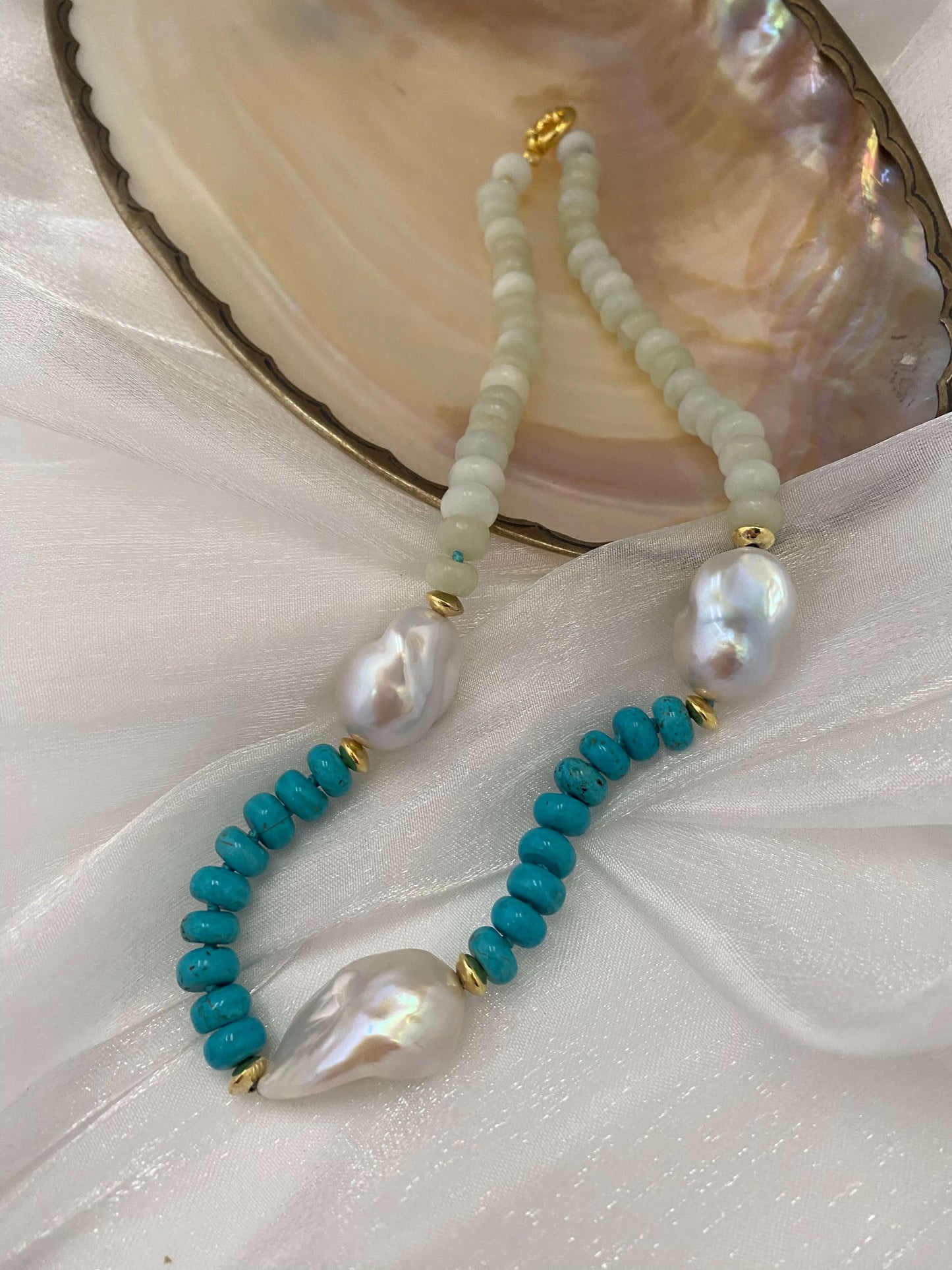 Close-up of green jade and turquoise pearl necklace on white shell backdrop
