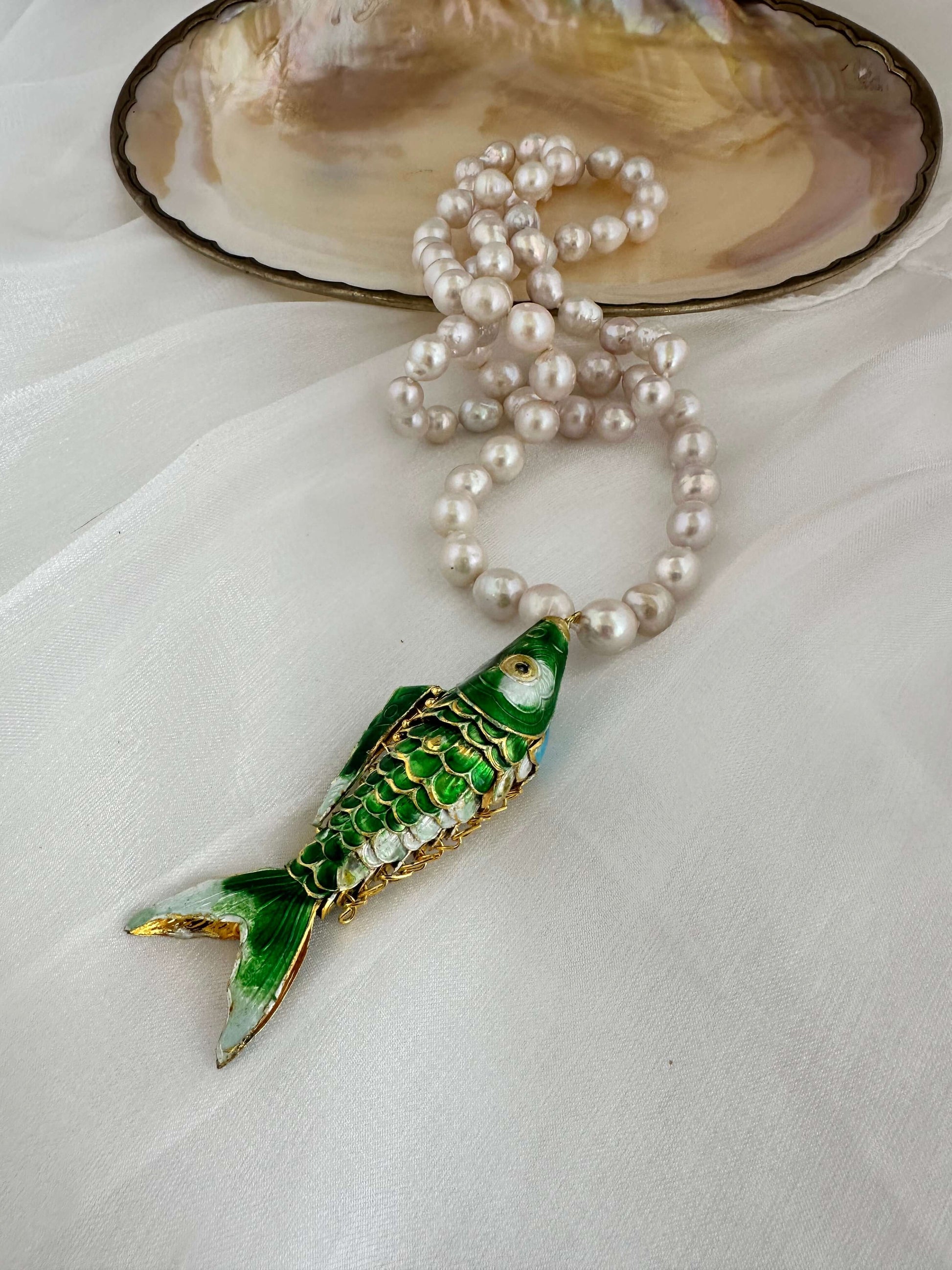 Cloisonné fish pearl necklace featuring green fish pendant and hand knotted baroque pearls on soft fabric background
