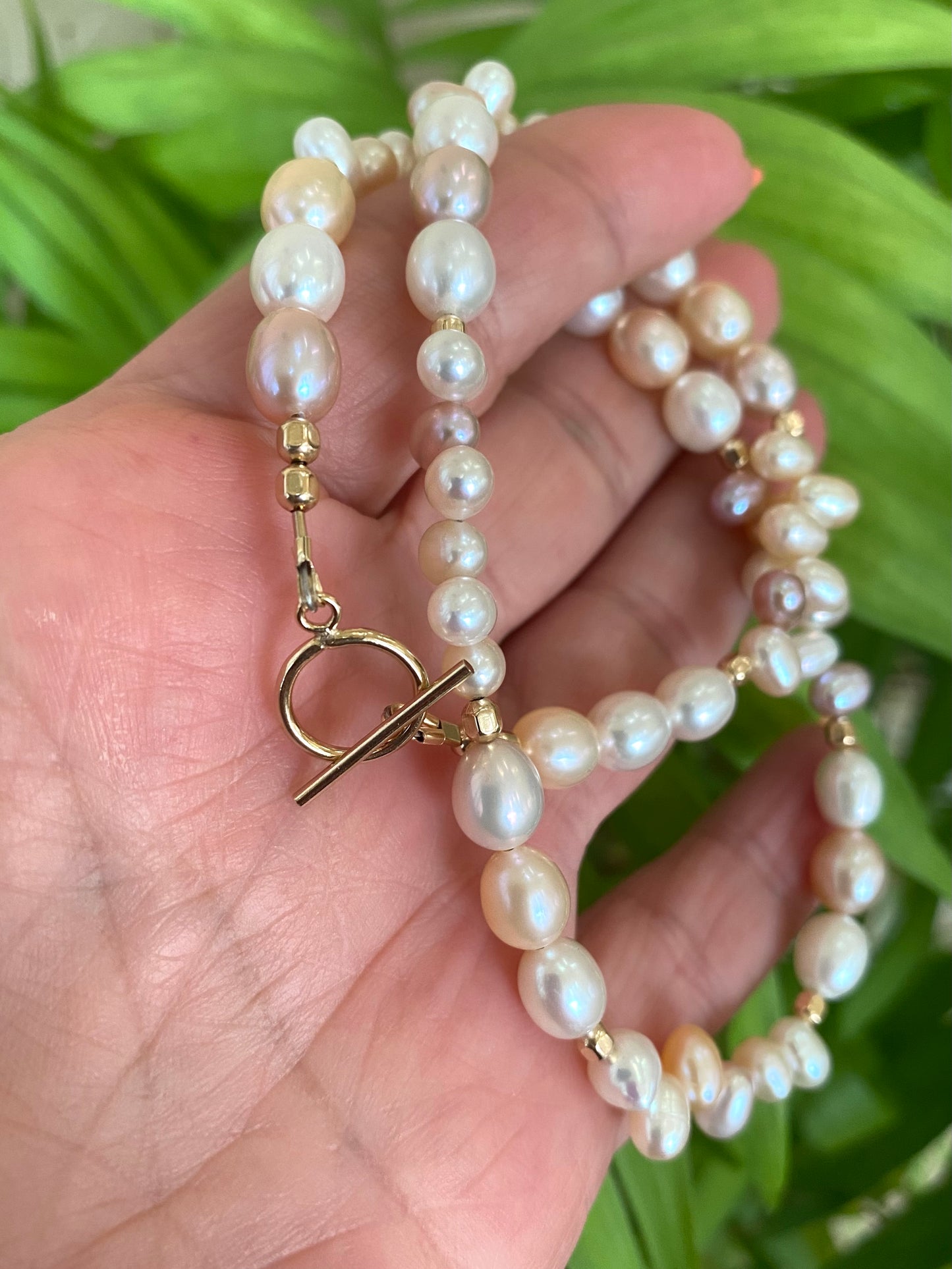 Pearl toggle necklace with pastel pearls and 14K gold filled clasp held in hand.