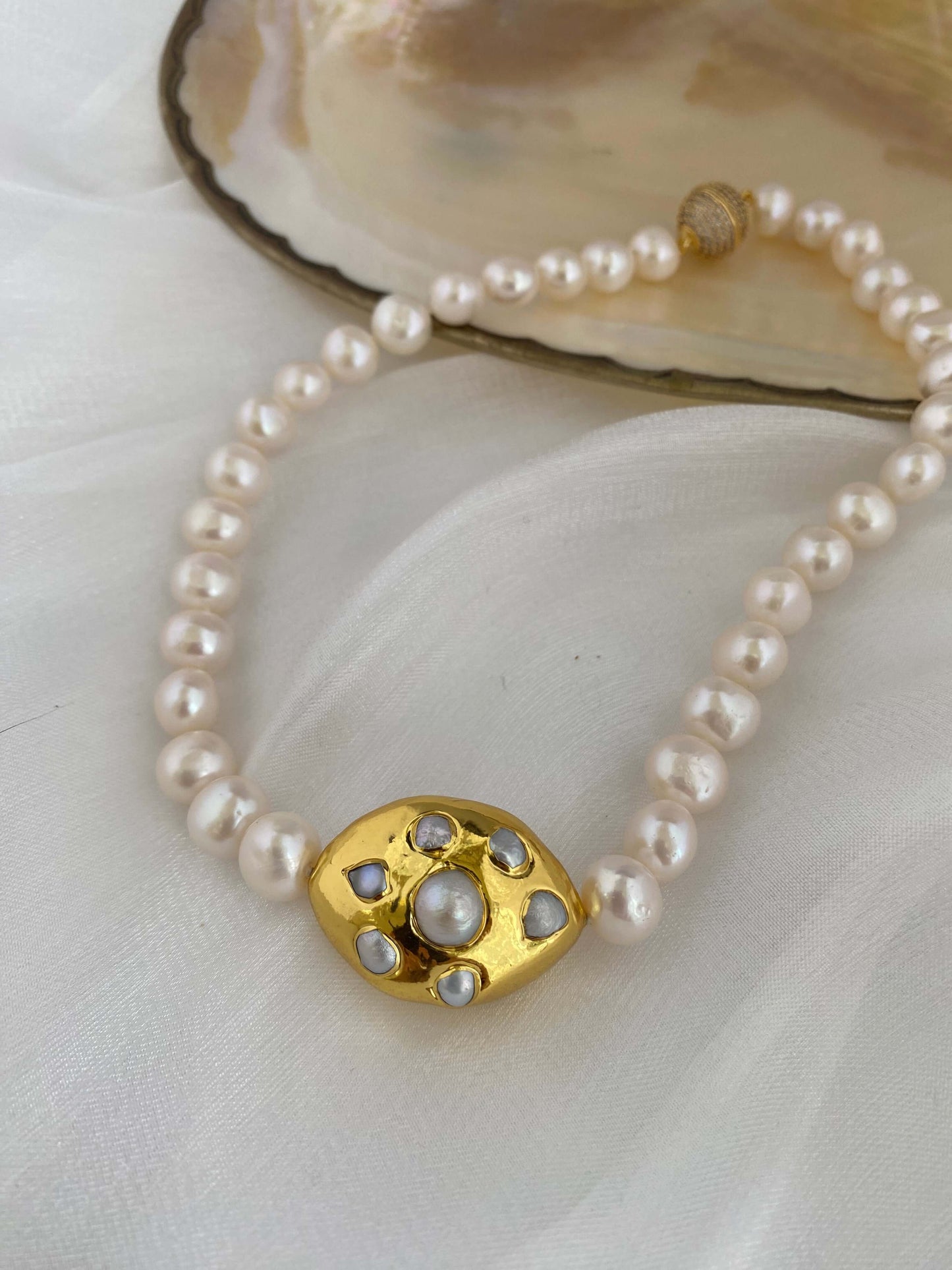 White potato pearl necklace with gold focal accent showcased on a soft backdrop, emphasizing its elegant design and natural beauty.