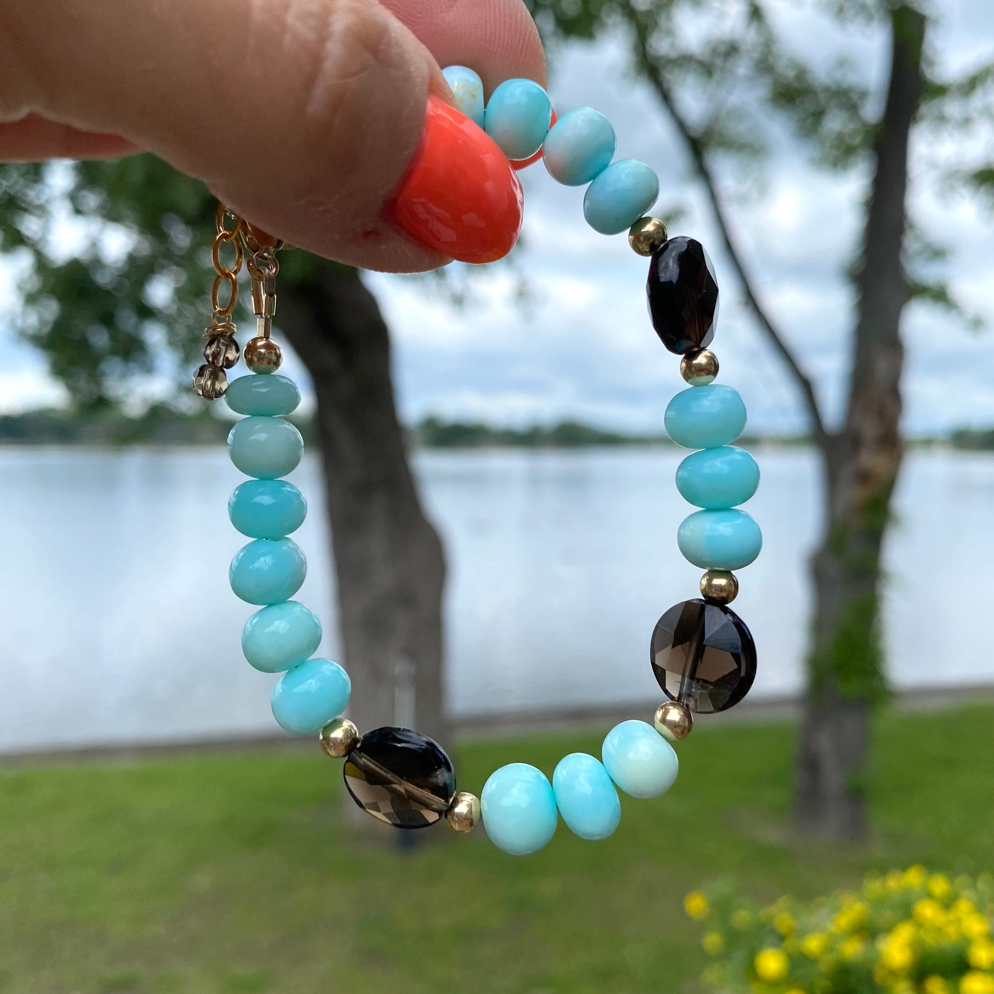 Opal quartz bracelet featuring sky blue opal and smoky quartz beads, held against a scenic lake background.