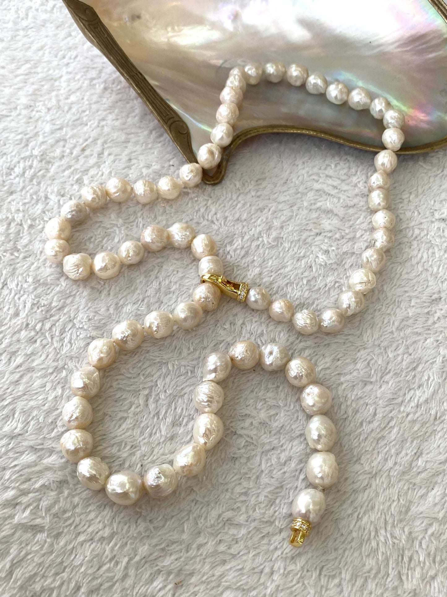 Edison pearl Y necklace featuring hand knotted white avocado baroque pearls on a soft surface with an iridescent shell.