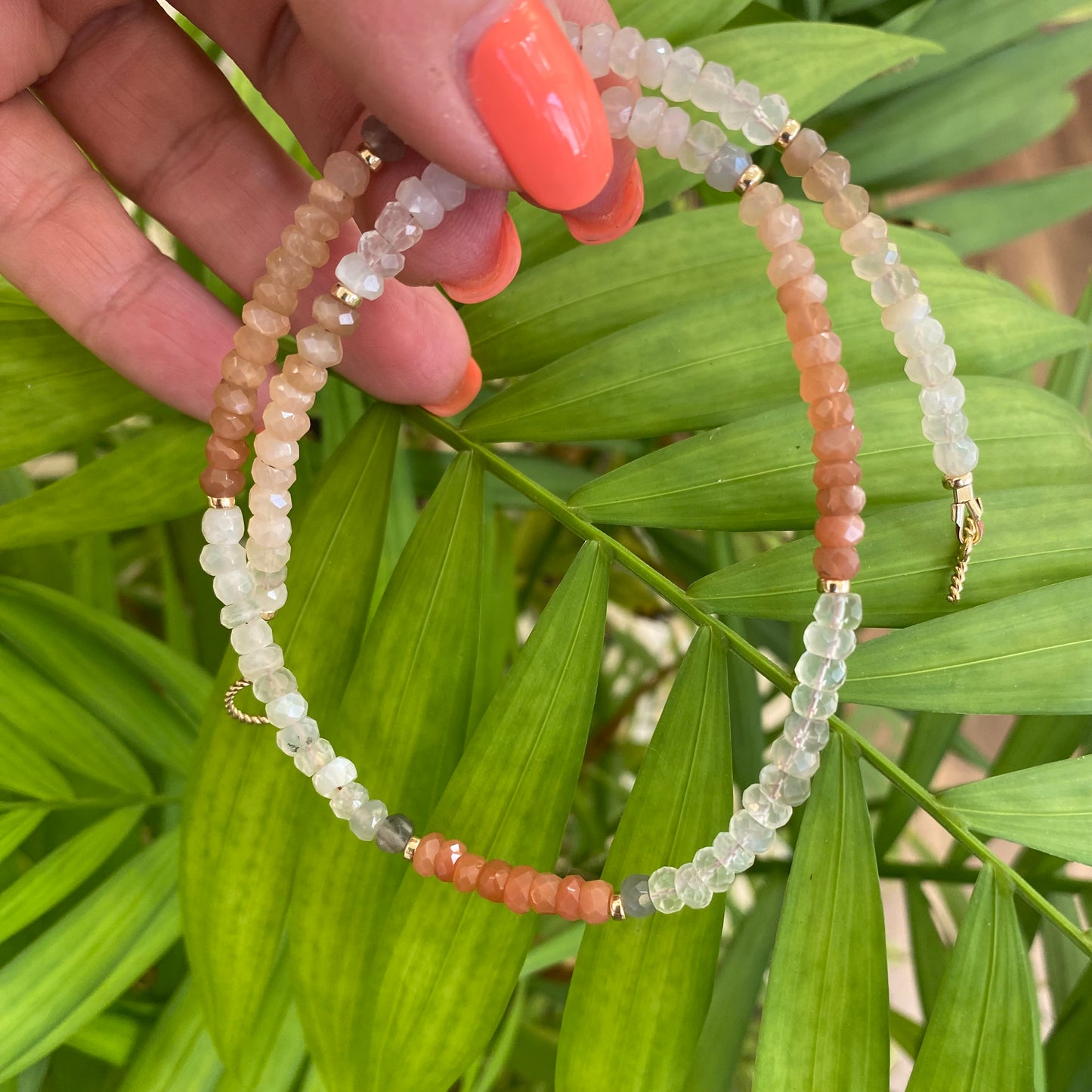 Moonstone choker necklace featuring multi moonstone beads in shades of blue, white, and rainbow tones against green leaves.