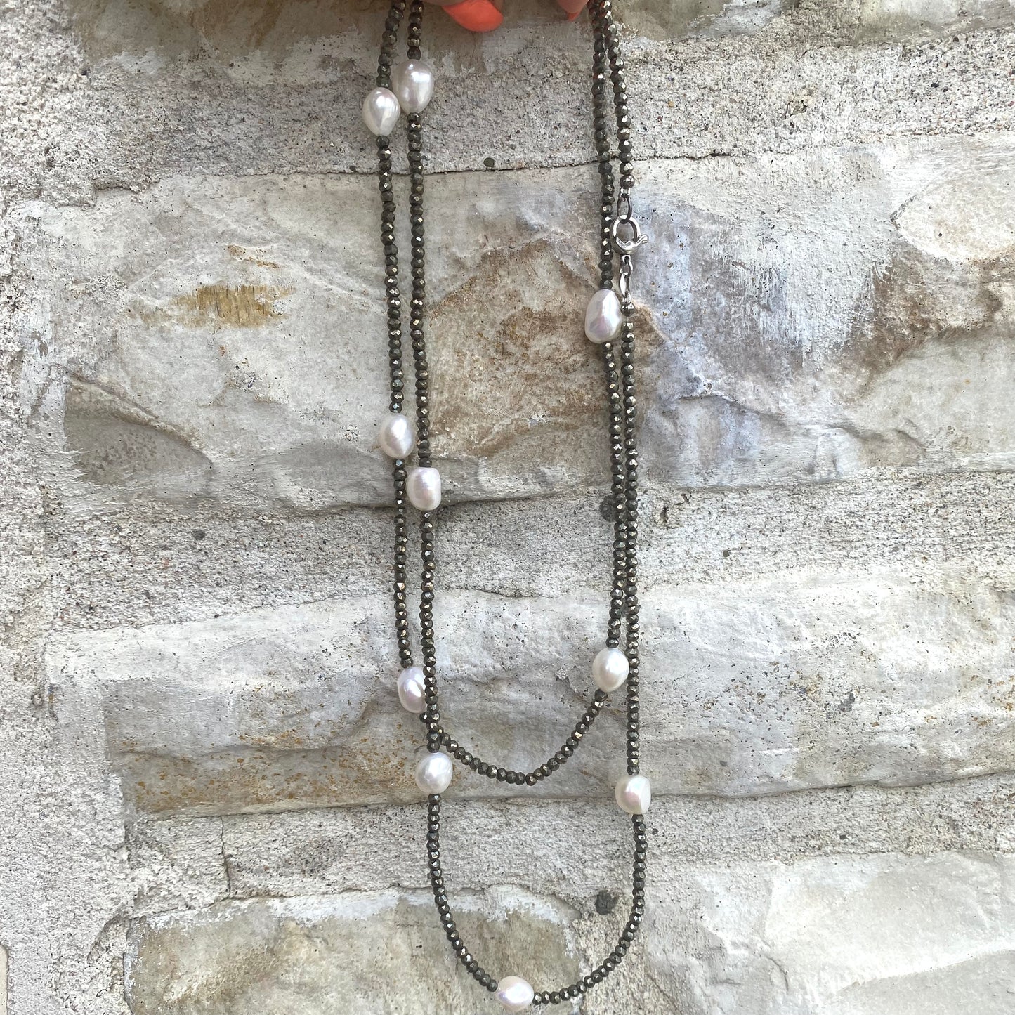 Handcrafted pyrite pearl long necklace featuring faceted pyrite beads and freshwater pearls against a stone backdrop.