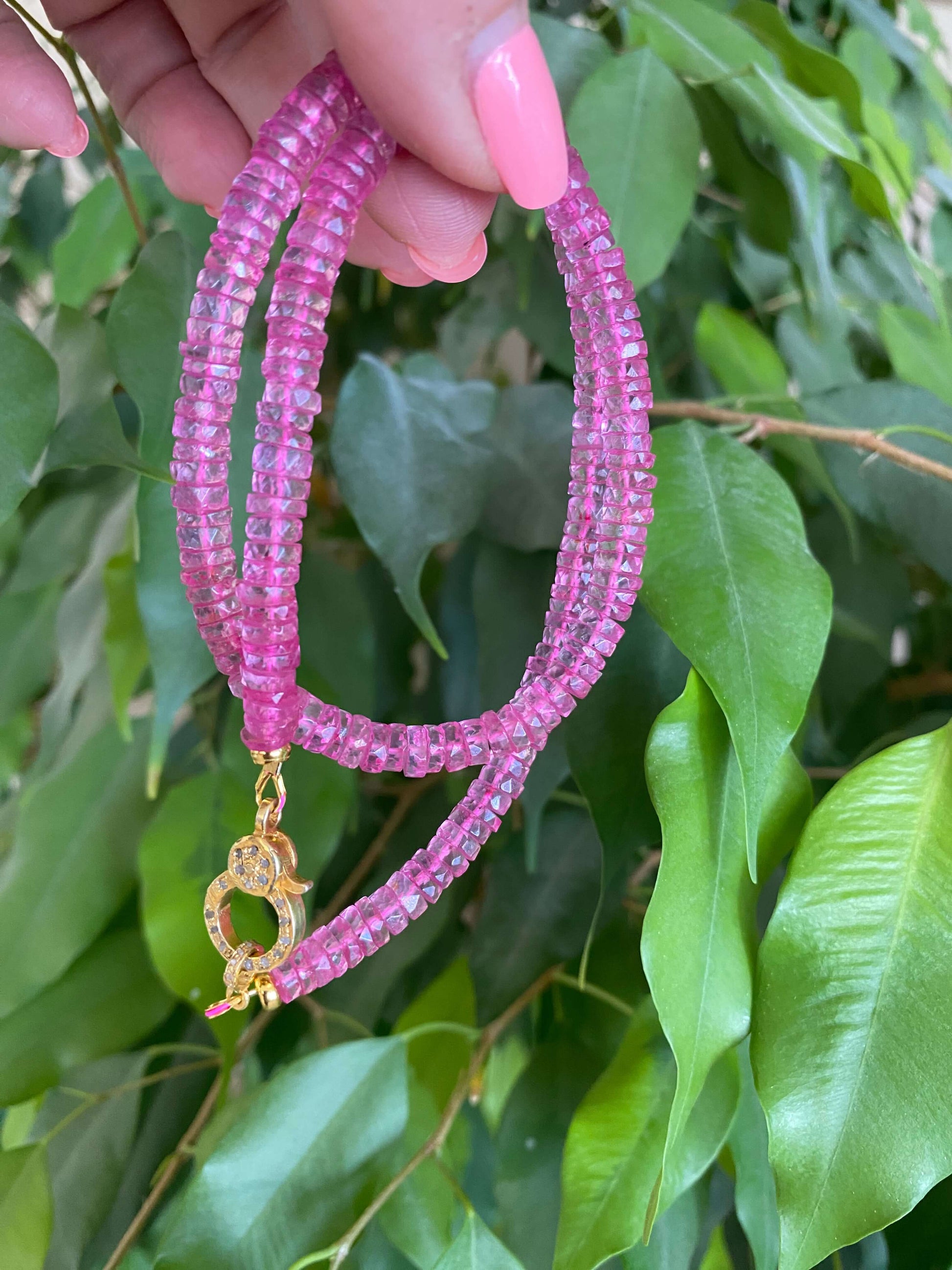 Pink topaz beaded necklace with gold vermeil pavé clasp displayed against green foliage.