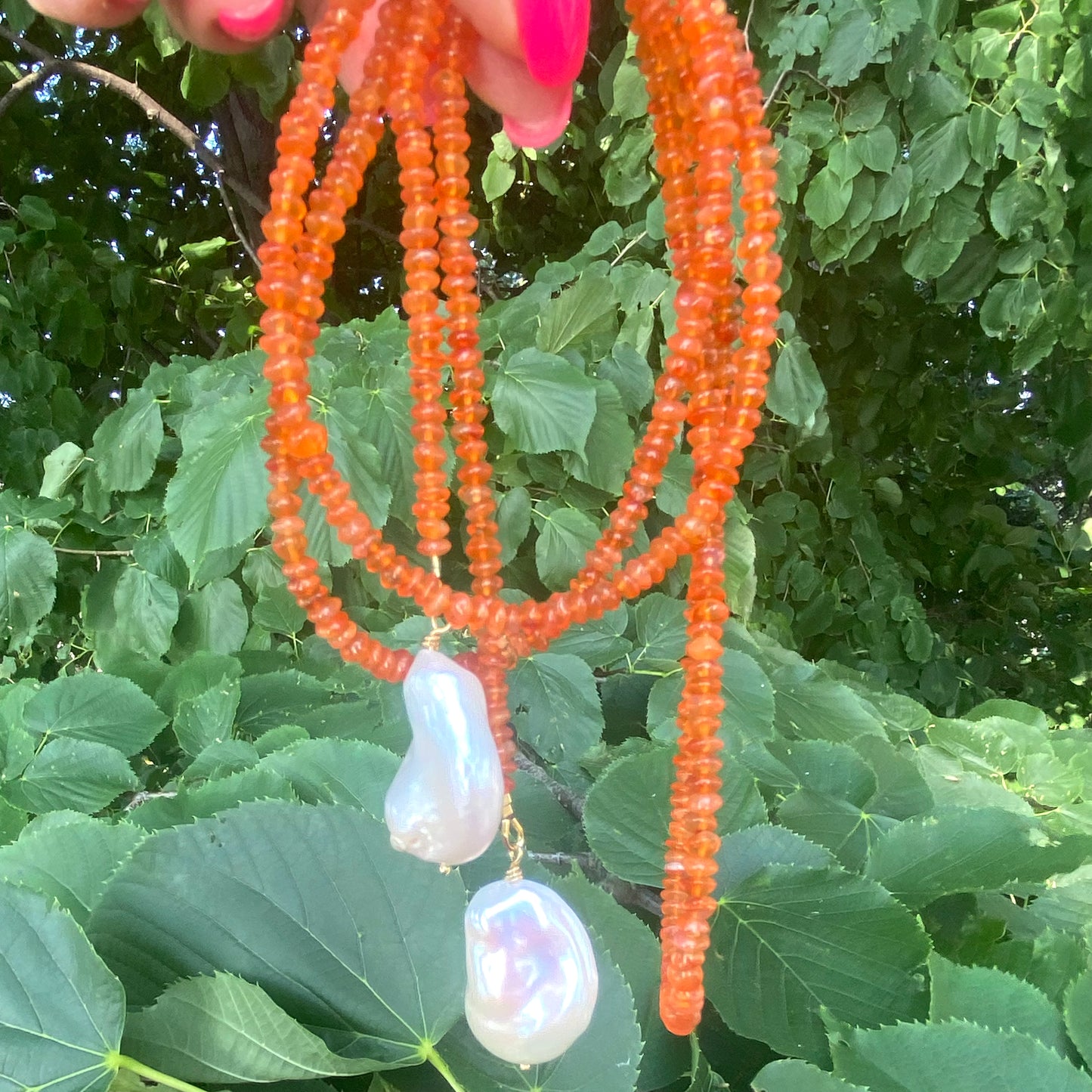 Carnelian lariat necklace with two baroque pearls, showcasing vibrant orange beads and organic textures.