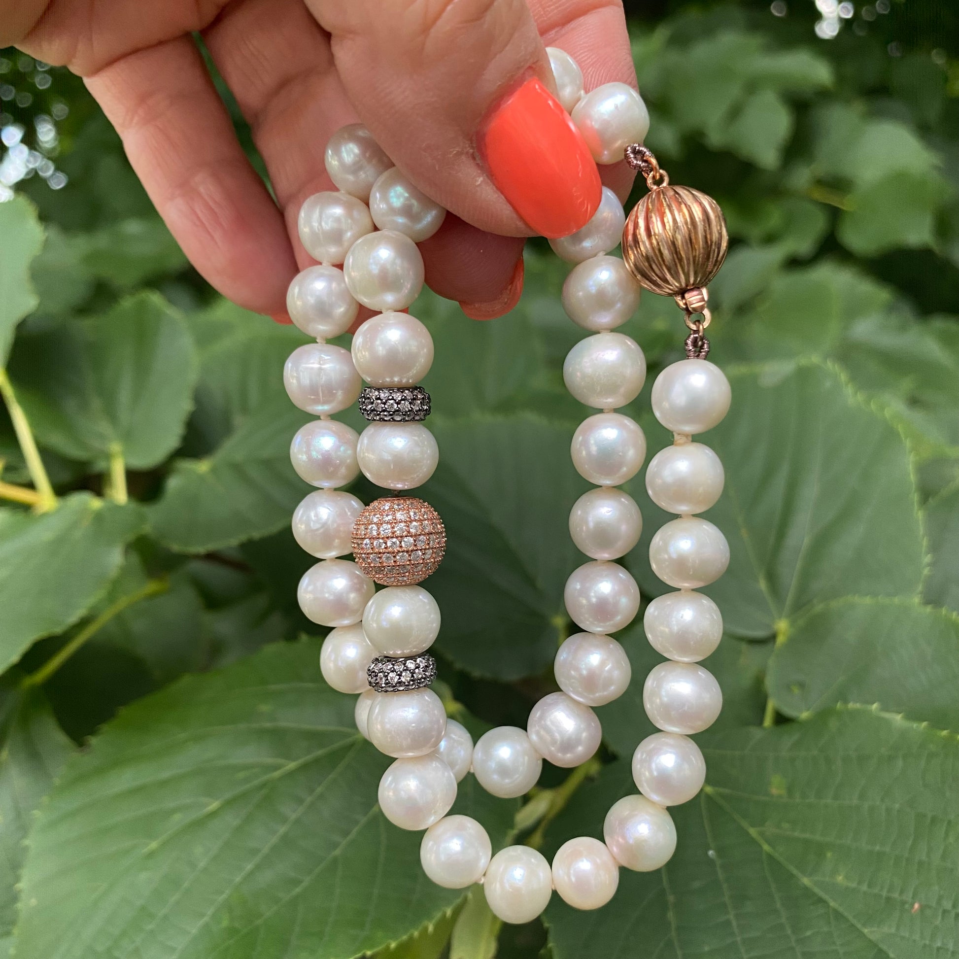 Rose gold pearl necklace with CZ pavé held in hand against green leaf backdrop, close-up view.