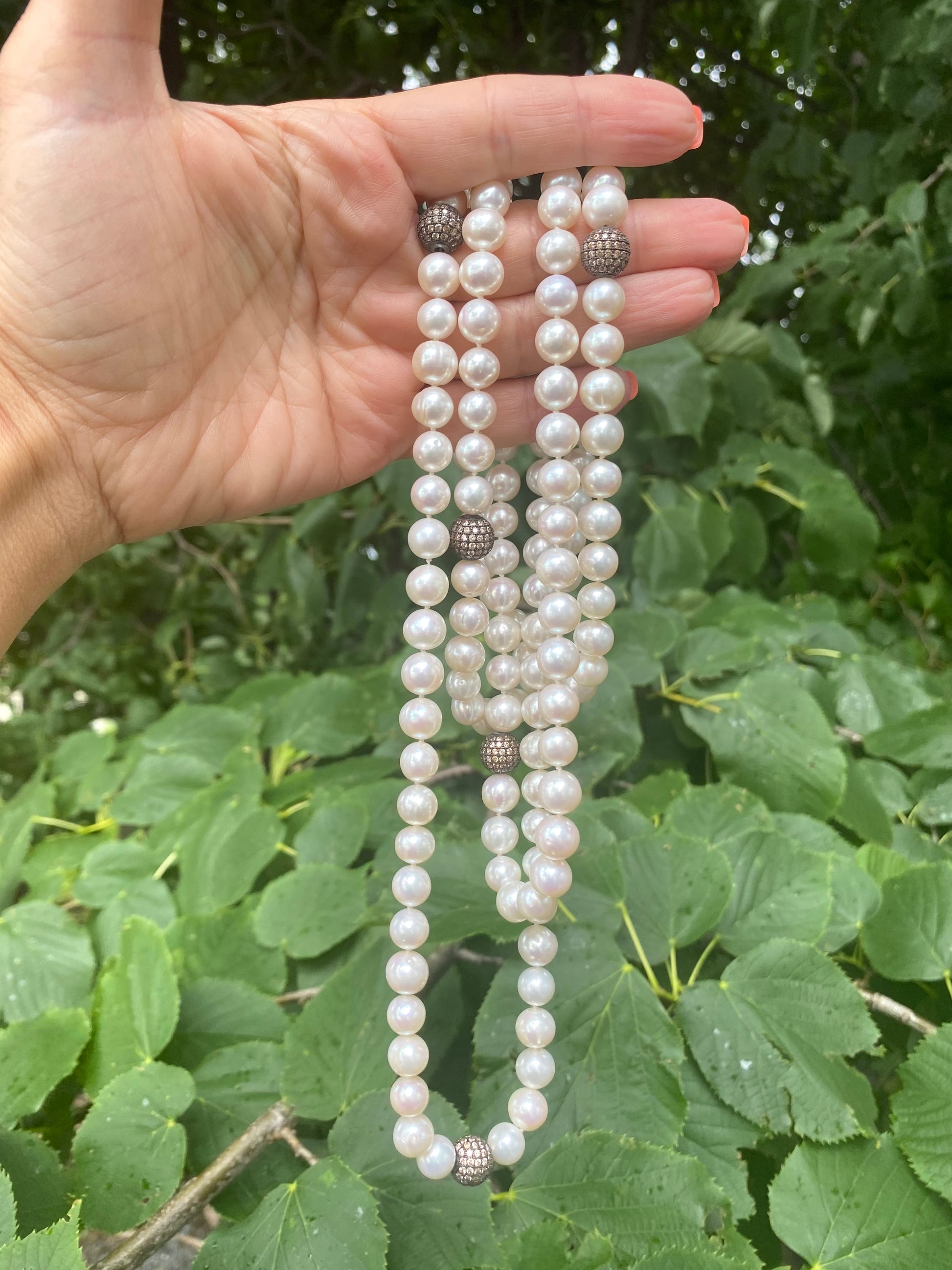 Handcrafted freshwater pearl necklace held against green leaf backdrop, handmade in Canada.