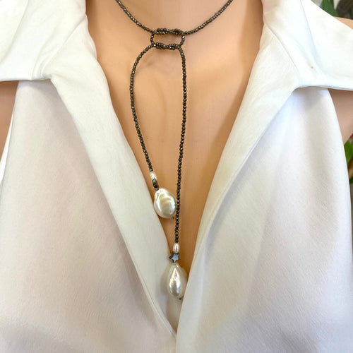 Hematite and pearl beaded lariat Y necklace featuring a single strand of tiny hematite beads, adorned with a hematite star and a baroque pearl at each end. In 27 to 32 inches, this elegant and versatile necklace adds a unique touch to any outfit.