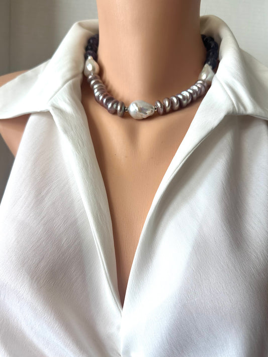 A close-up of a beaded necklace displayed on a mannequin torso wearing a white collared blouse. The necklace features a mix of dark PURPLE cord, silver-toned beads, and a prominent white pearl-like bead at the center.