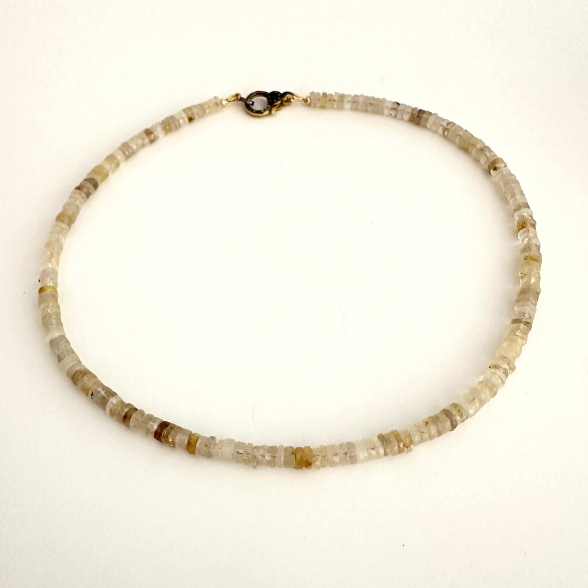 A beaded necklace made of small, chunky translucent stone beads in shades of beige, cream, and light brown, with a small gold clasp, shown on a plain white background.