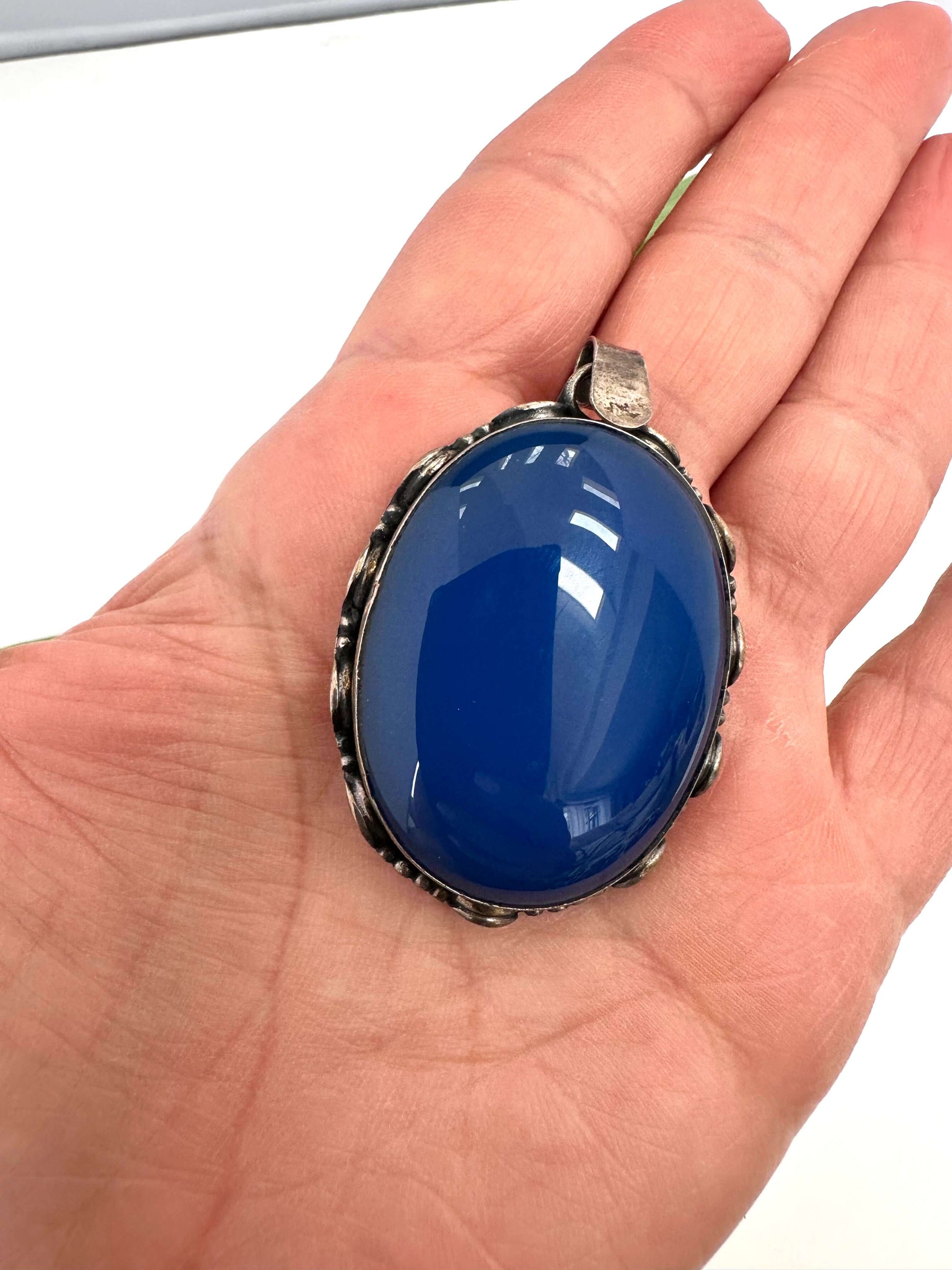 Vintage blue agate pendant in oxidized sterling silver held in hand, showcasing its deep cobalt hue and elegant design.