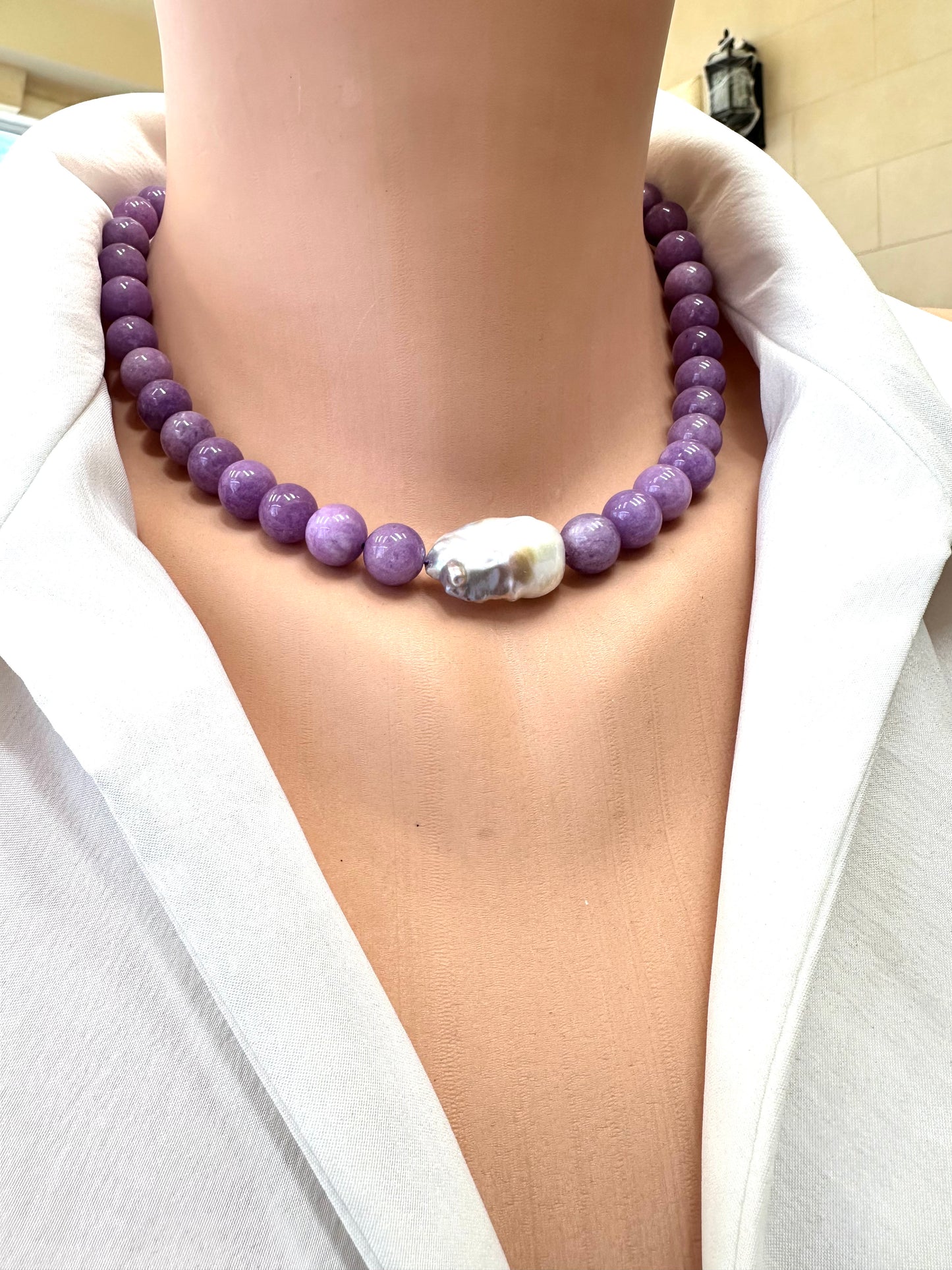 Purple beaded necklace with a large white pearl on a person wearing a white shirt.