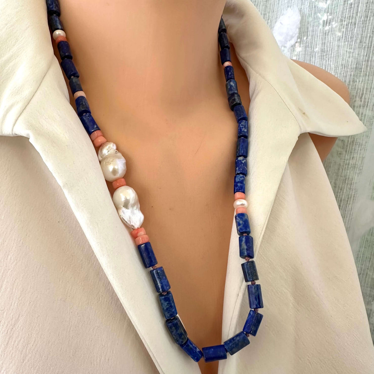 Lapis lazuli necklace with pink coral and baroque pearls worn by a mannequin, showcasing vibrant blue, pink, and lustrous accents.