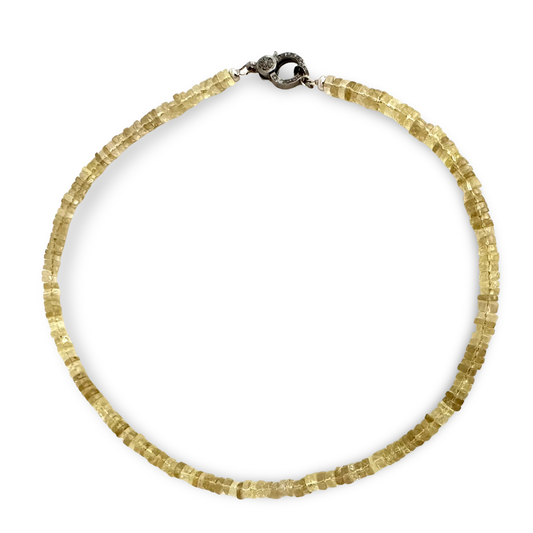 A beaded necklace made of faceted, translucent pale yellow lemon beads, arranged in a circle on a solid white background. It features a dark metal clasp at the top.