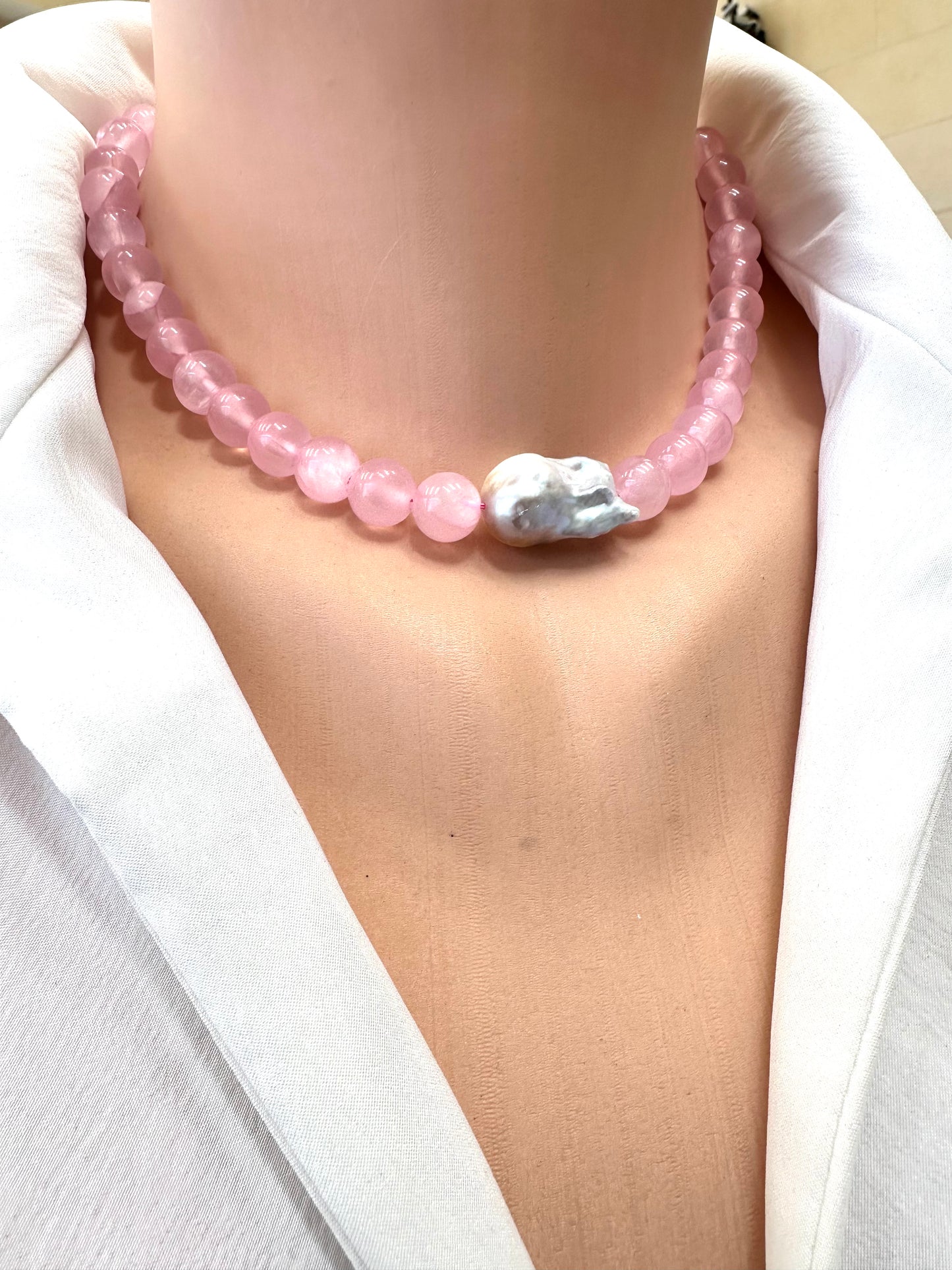 Pink beaded necklace with a silver pendant worn by a person in a white outfit.