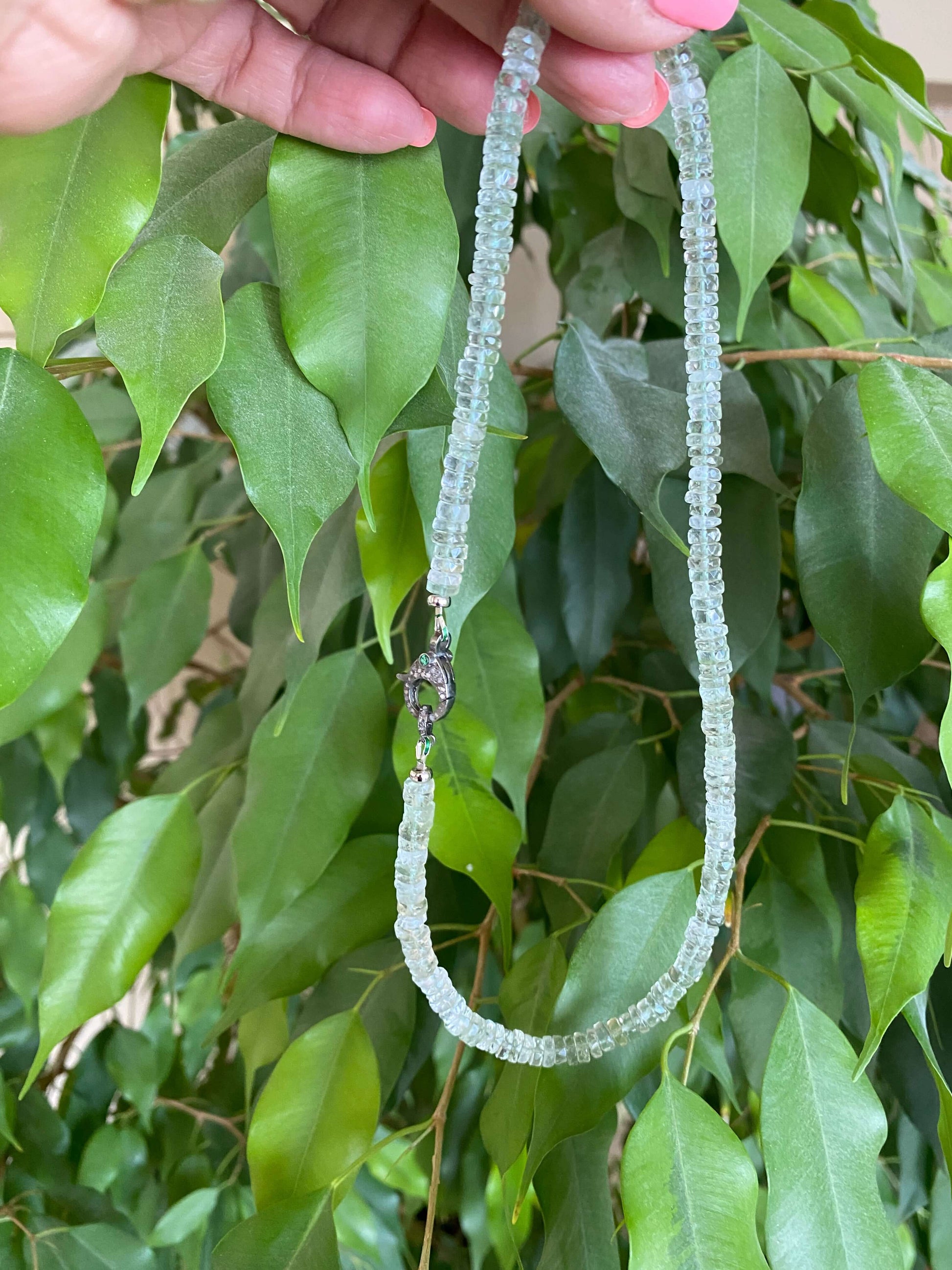 Green amethyst beaded necklace with diamond and emerald pavé clasp displayed against green foliage.