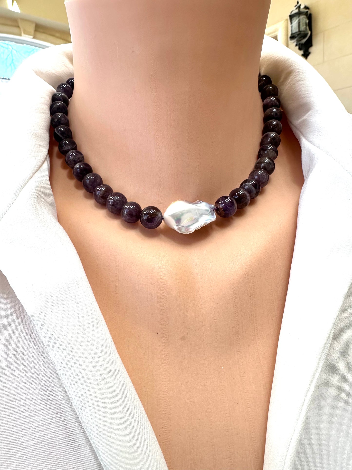 Necklace with dark beads and a large white stone worn by a person in a white outfit.