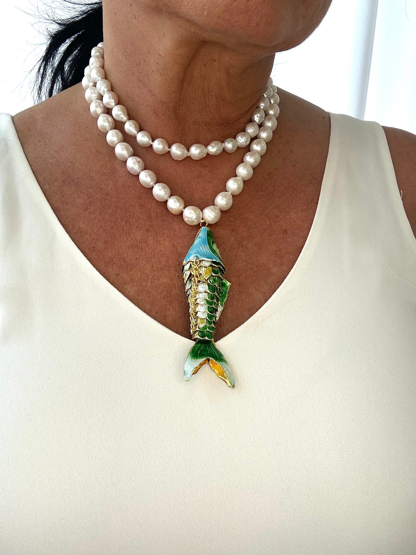 Pearl necklace with a fish-shaped pendant worn by a person on a white background