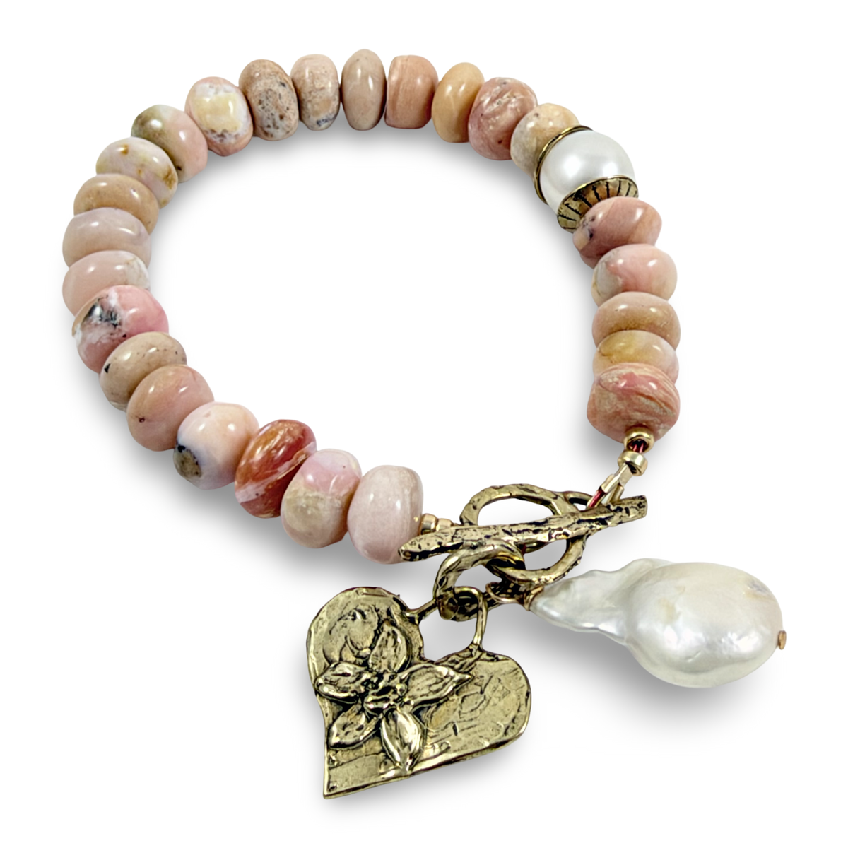 A beaded stretch bracelet featuring polished pink and beige stone beads, a white pearl accent, and a toggle clasp with a gold-tone heart charm and a baroque pearl drop, shown on a white background.