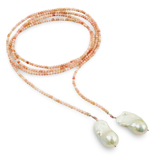 A long beaded necklace with multiple strands of small peach, pink, and cream beads leading to two large, irregular baroque-style white pearls at the ends, shown on a plain white background.
