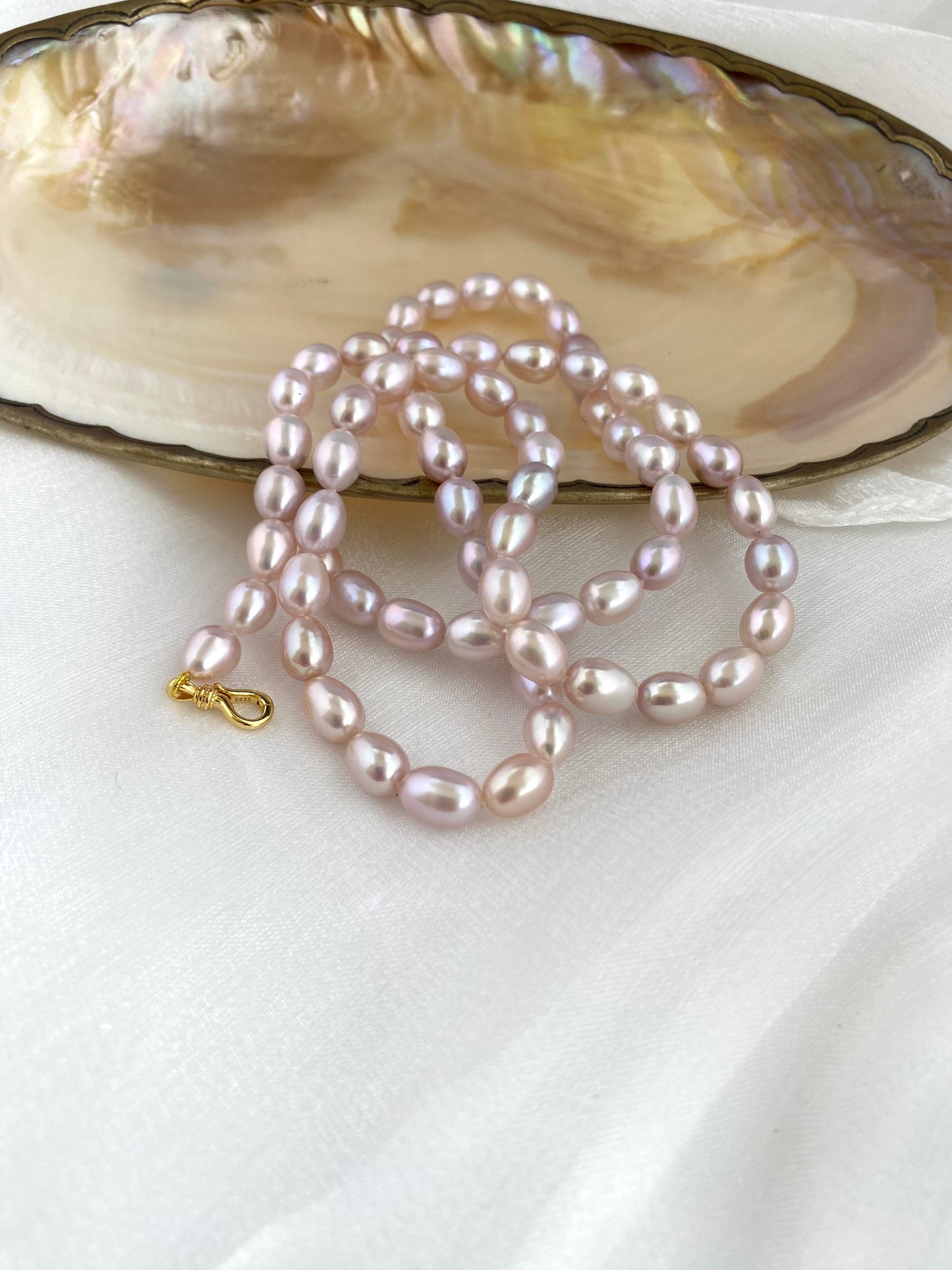 Pearl necklace on a white surface with an open shell in the background