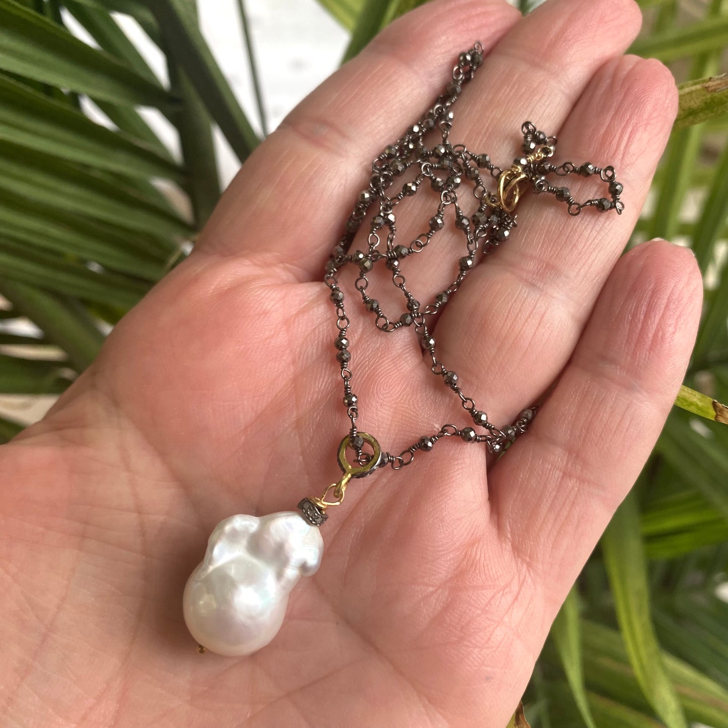 Pyrite rosary chain necklace held in hand against green foliage, close-up in natural light