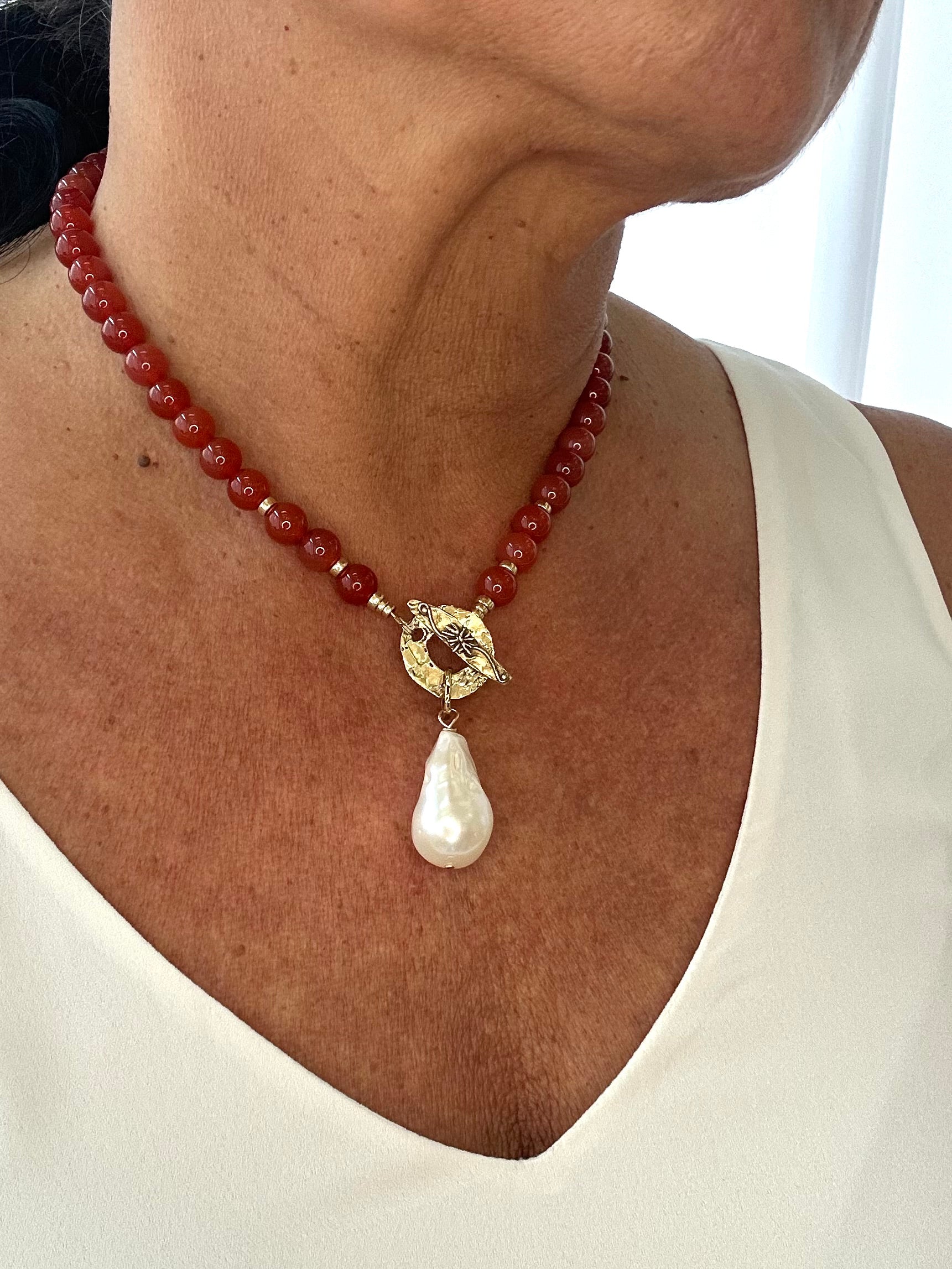 RED AGATE NECKLACE WITH ARTISAN TOGGLE CLASP AND BAROQUE PEARL PENDANT WORN BY A PERSON