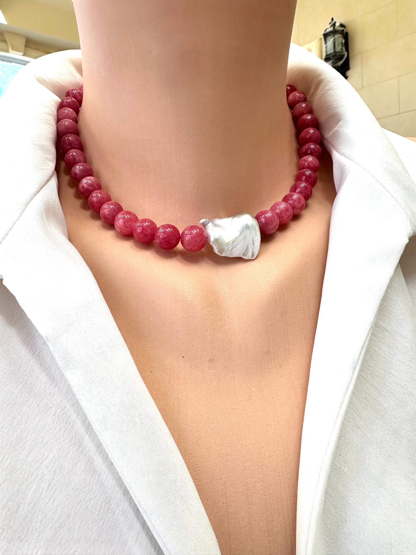 Person wearing a red beaded necklace with a silver clasp against a white shirt.