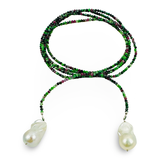 A long strand beaded necklace featuring vibrant green and deep purple beads, with two large, irregular white baroque pearls hanging from the ends, set against a plain white background.