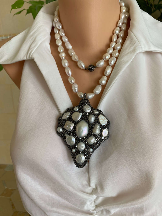 Close-up of a pearl brooch and necklace on a white blouse.