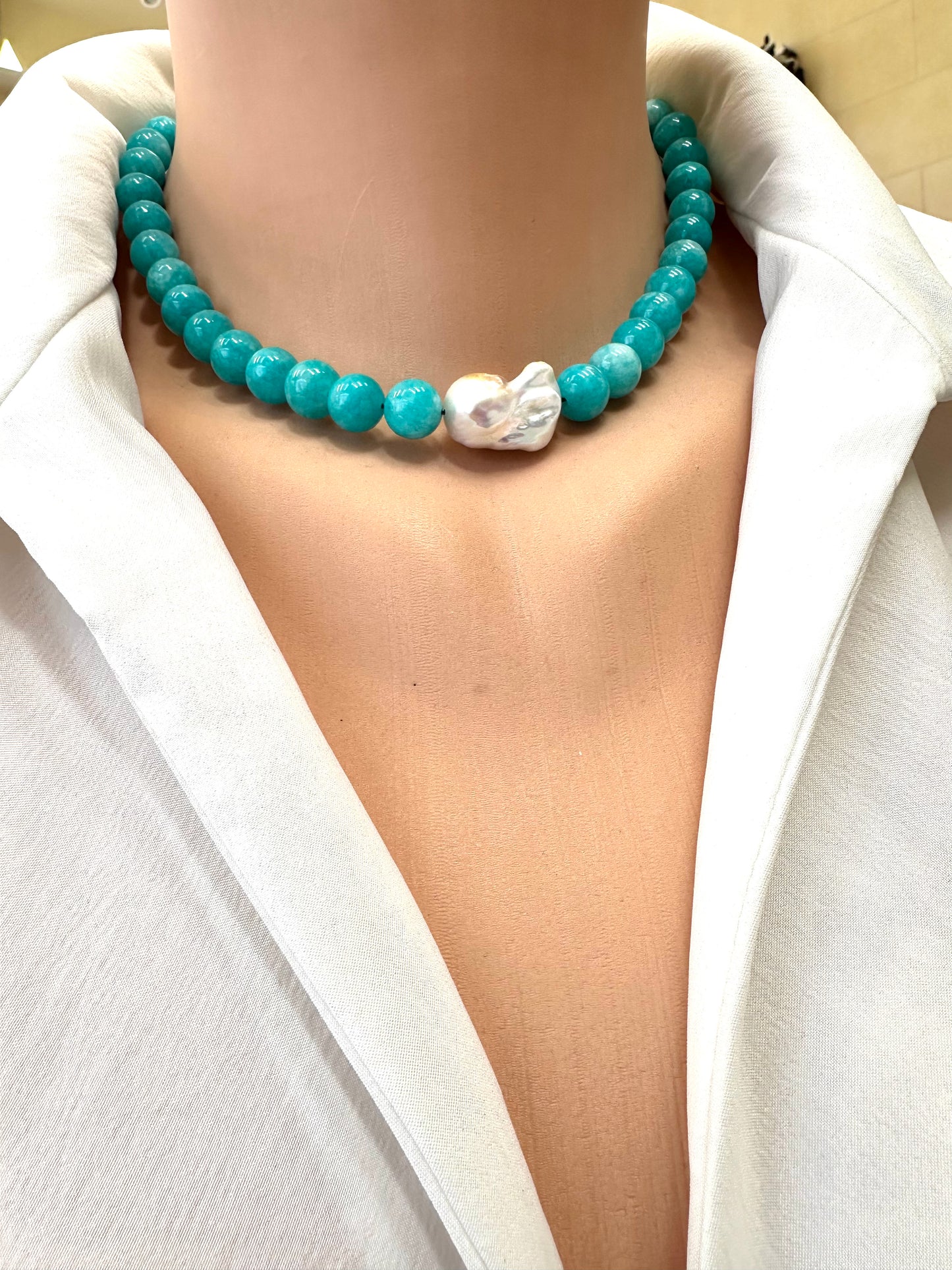 Turquoise beaded necklace with a white pendant on a person wearing a white shirt.