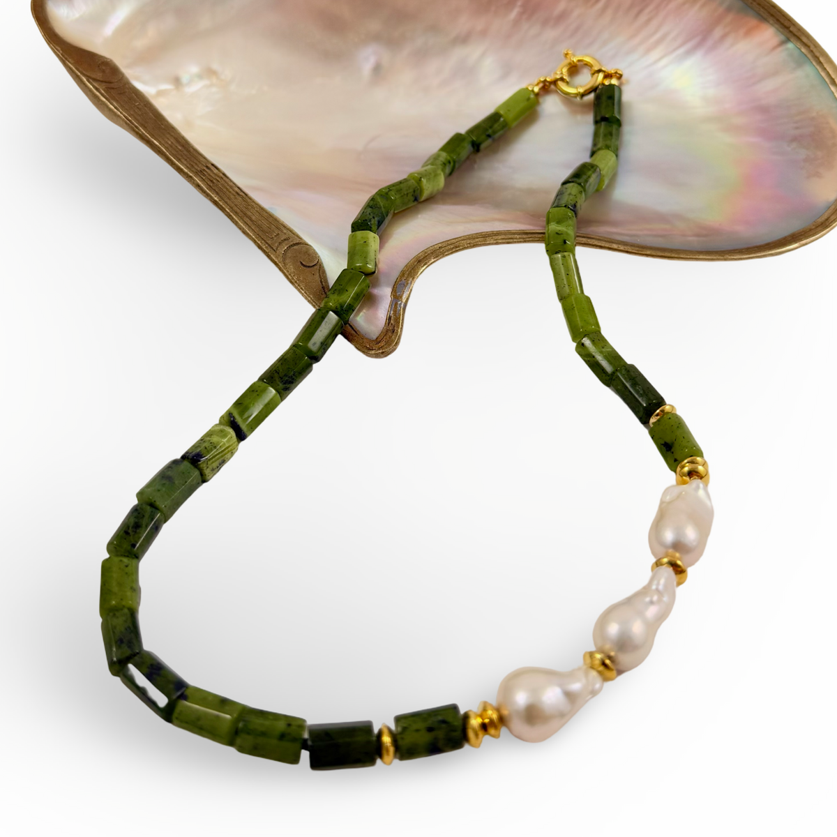 A beaded necklace with faceted green beads, a section of irregular white pearls, and small gold spacer rings, displayed on a white background with a mother-of-pearl shell prop.