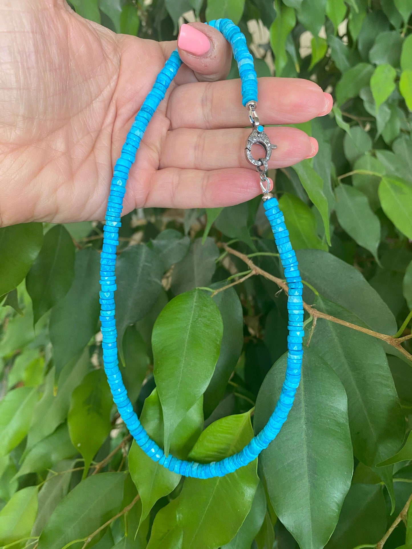 Turquoise howlite beaded necklace shown in hand among green leaves with oxidized silver clasp.