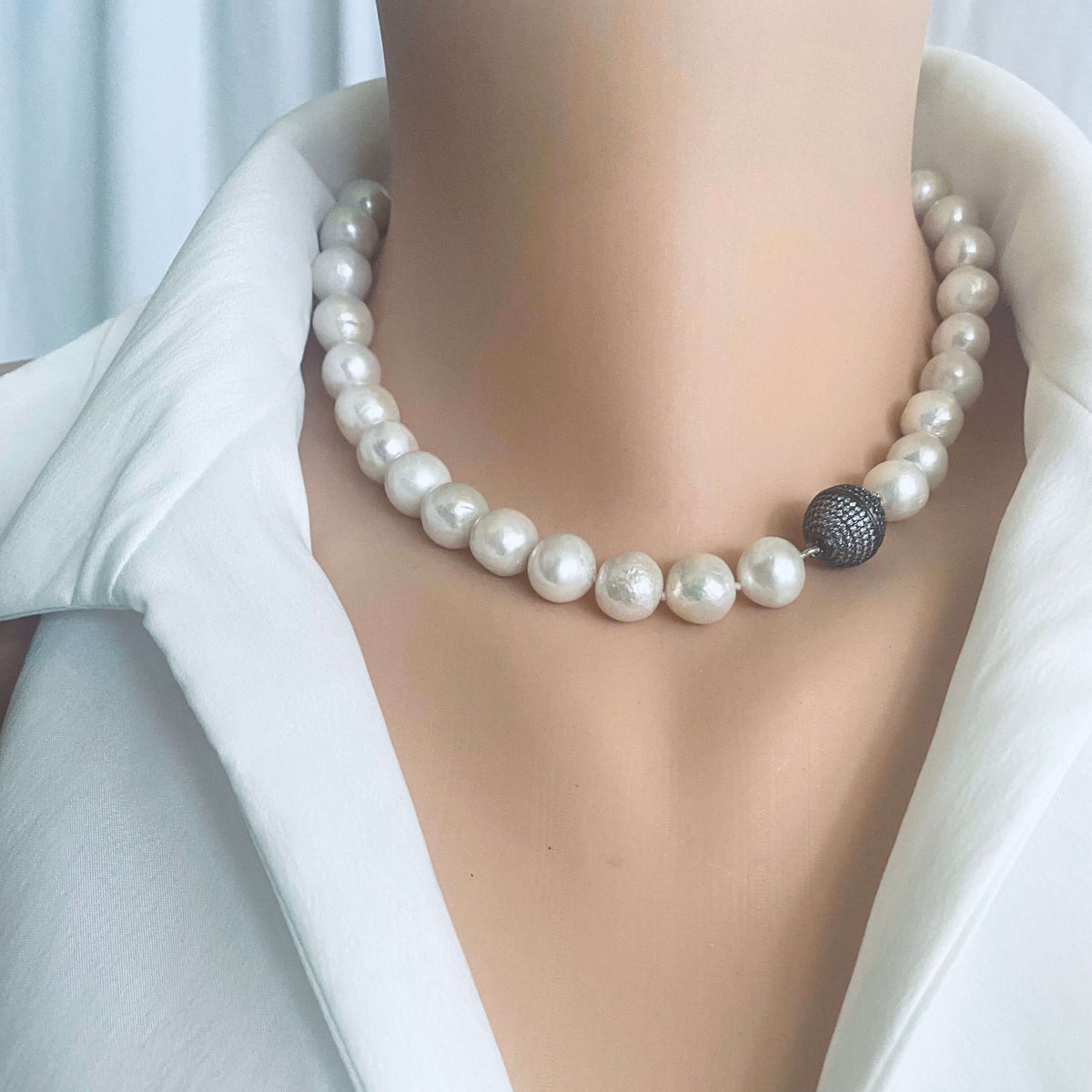 White Edison pearl necklace with gunmetal pavé magnetic clasp worn around the neck, featuring large luminous round pearls.