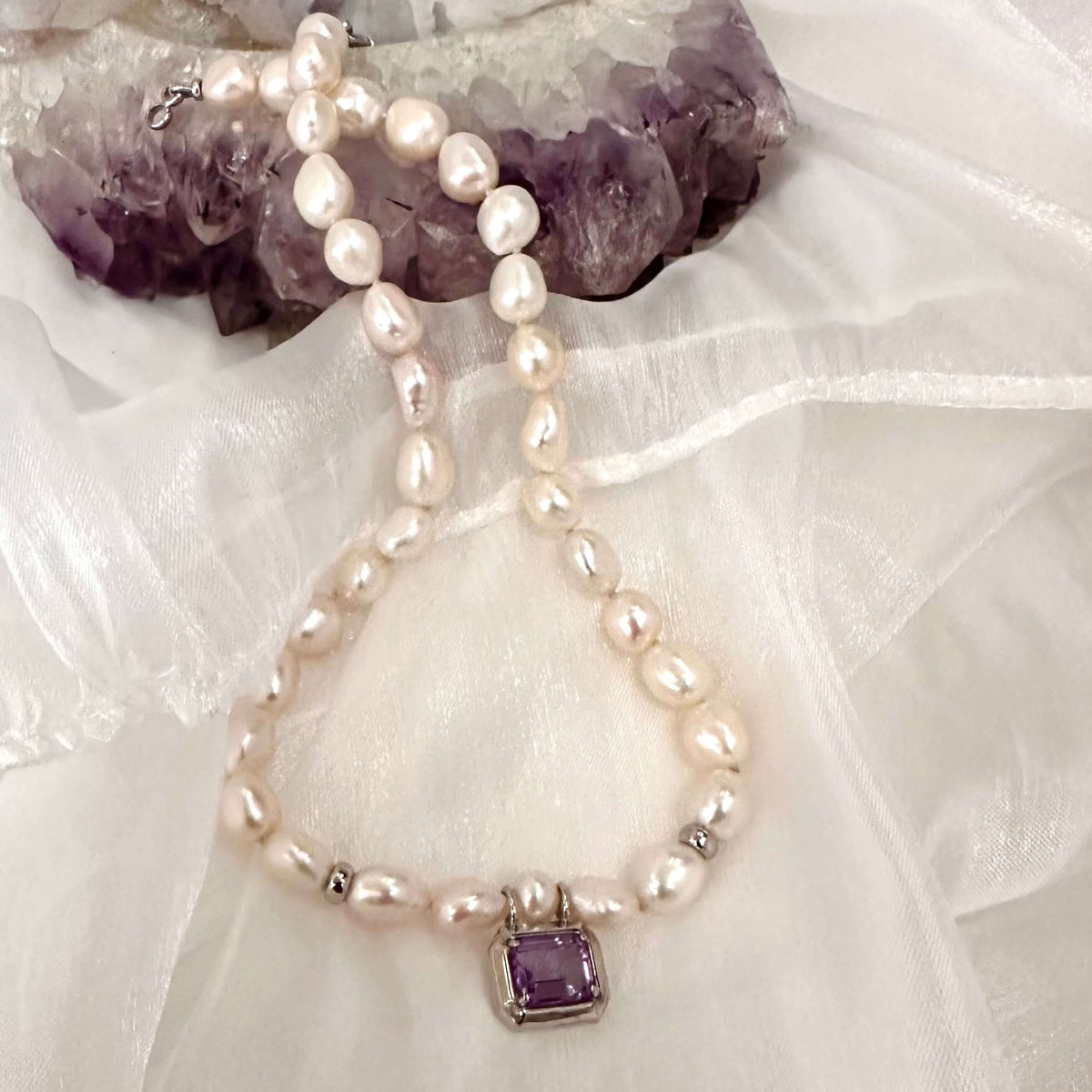 White Nugget Pearl Necklace with Amethyst Pendant – 'Viola' Collection on a soft fabric background.