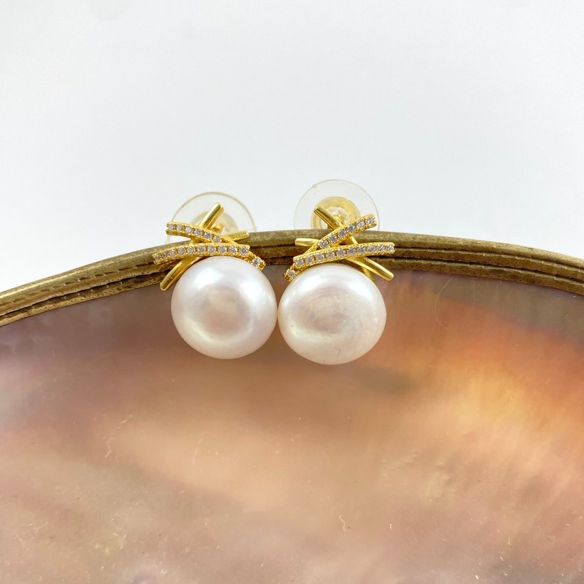 a pair of freshwater pearl earrings studs in gold vermeil on a shell background
