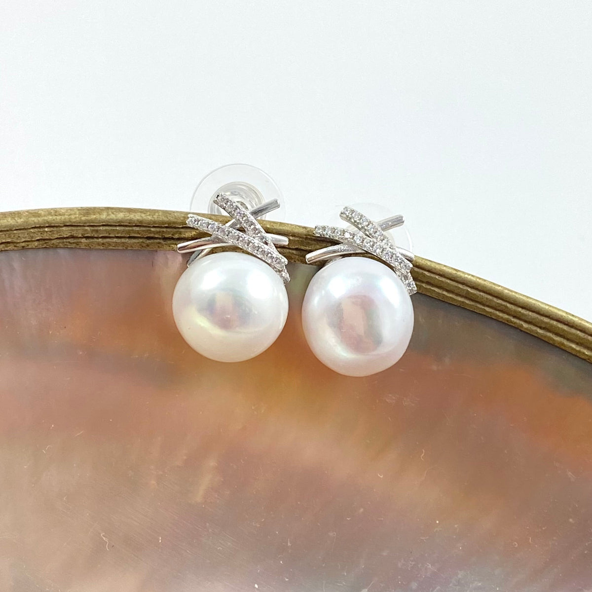 a pair of freshwater pearl earrings studs in silver on a shell background