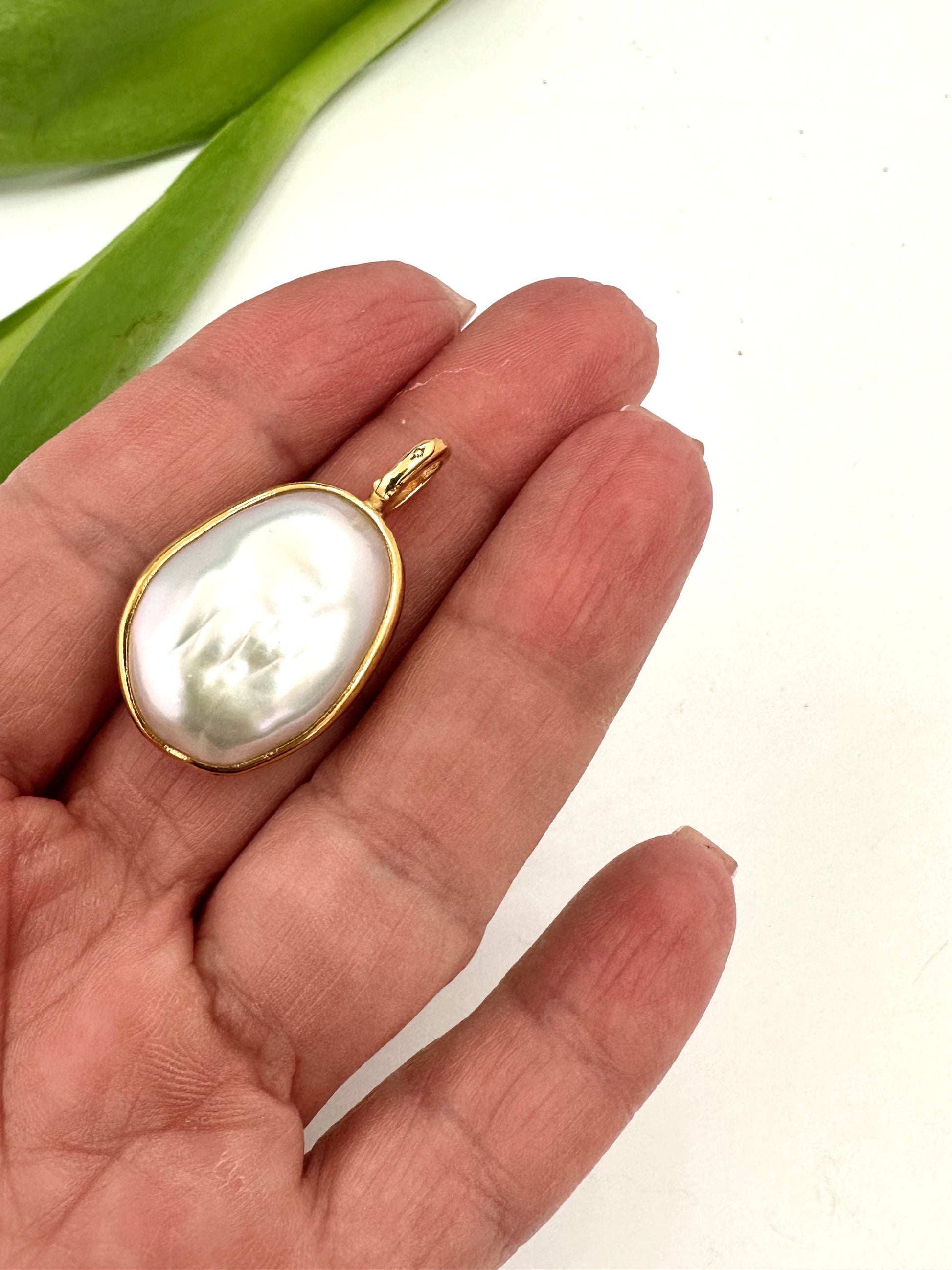 Gold pendant with a pearl on a hand against a white background