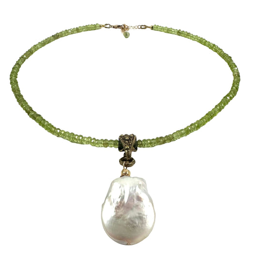 A beaded necklace featuring a strand of light green faceted beads, a bronze-toned central connector, and a large, irregular white baroque pearl pendant, displayed on a clean white background.