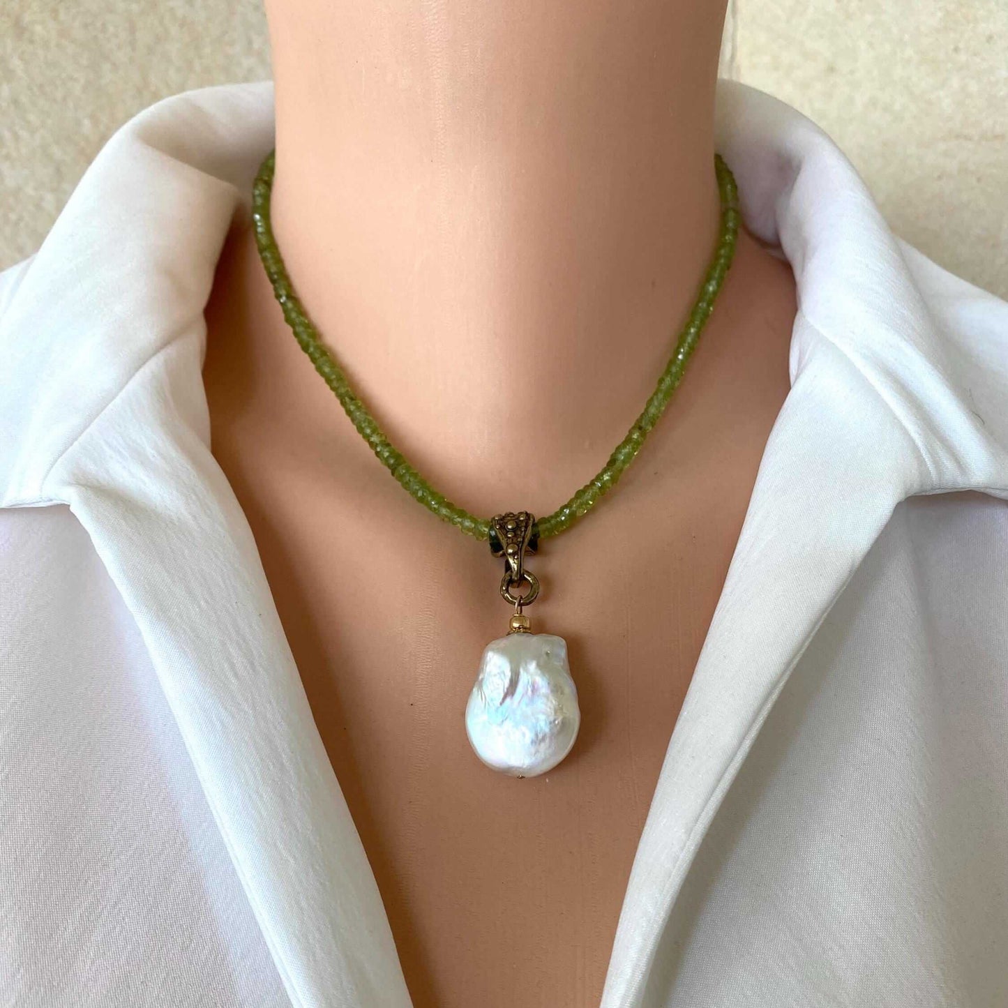A close-up of a person wearing a green beaded necklace with a large, irregular white baroque pearl pendant, styled with a white collared shirt.