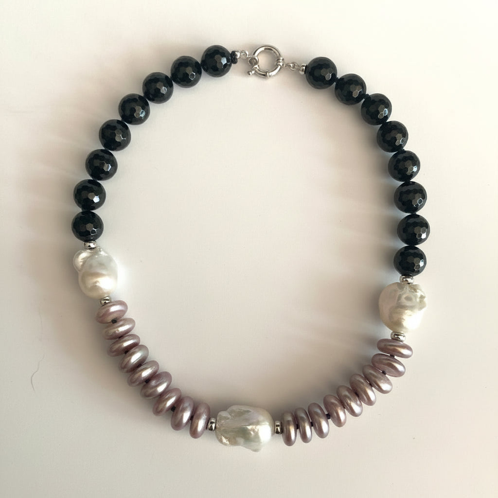 A beaded necklace featuring black faceted round beads, irregular white pearl-like beads, and textured mauve-pink spiny oyster shell beads, displayed on a light off-white background.