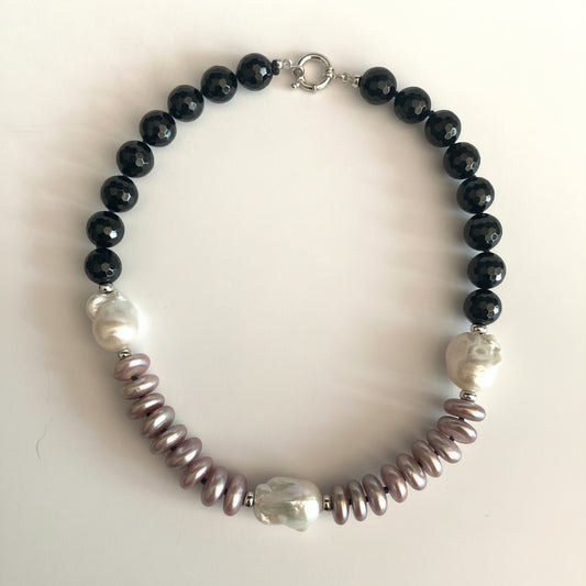 A beaded necklace featuring black faceted round beads, irregular white pearl-like beads, and textured mauve-pink spiny oyster shell beads, displayed on a light off-white background.