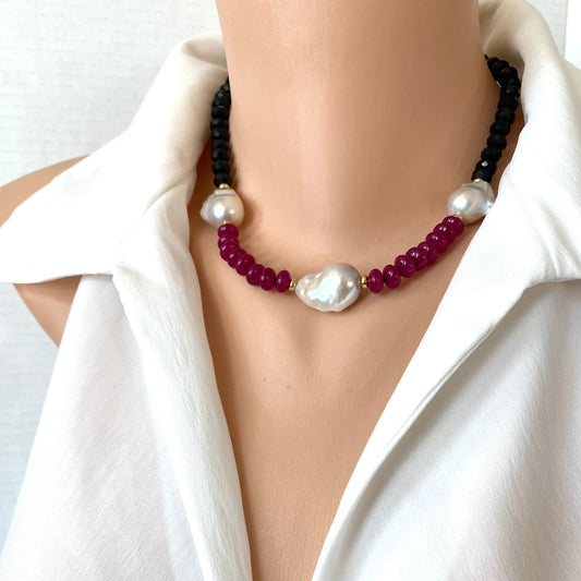 A close-up of a beaded necklace displayed on a mannequin torso wearing a white blouse, dark black beads with deep red beads, accented by white pearls.
