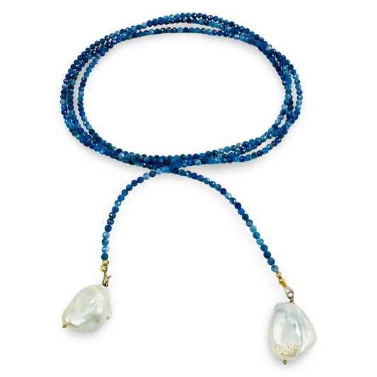 A beaded necklace featuring long strand of deep blue beads, and two large, irregular white baroque shell pendants, displayed on a clean white background.