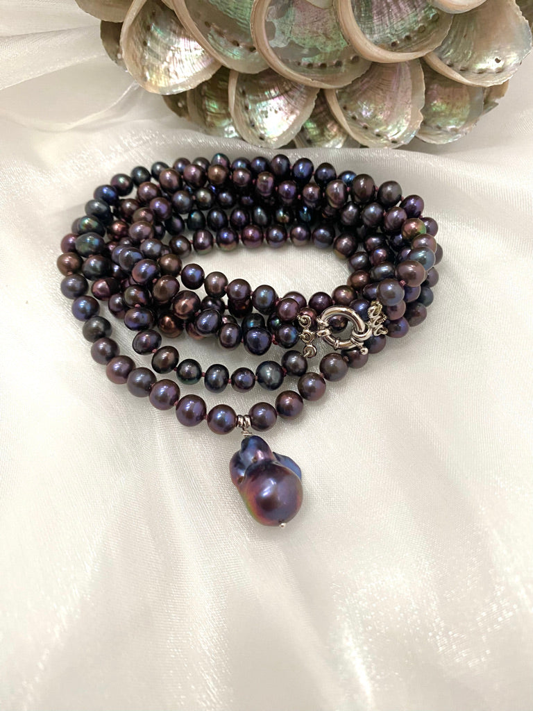 Pearl necklace with a large purple pearl pendant on a white surface