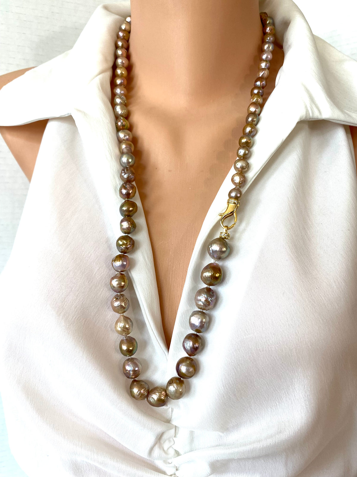 A long strand of large irregular freshwater pearls in a champagne, taupe, and brown gradient with a gold clasp, shown on a mannequin wearing a white collared blouse.