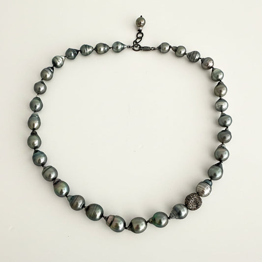 A dark gray baroque pearl necklace with a textured silver accent bead and a small silver clasp, displayed on a plain off-white background.