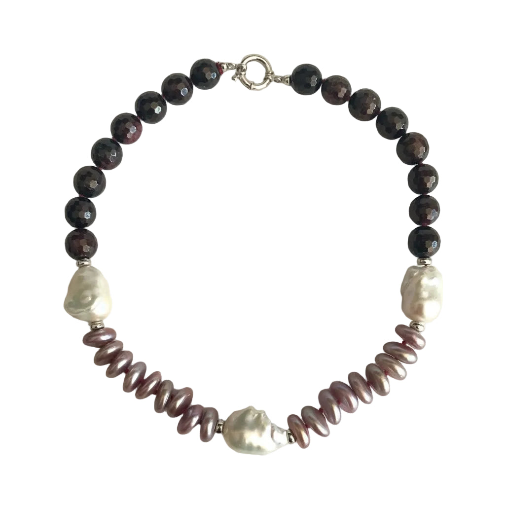 A beaded necklace featuring dark brown faceted beads, two white baroque pearls, and a row of iridescent mauve-pink spiral baroque pearls, finished with a silver clasp on a light beige background.